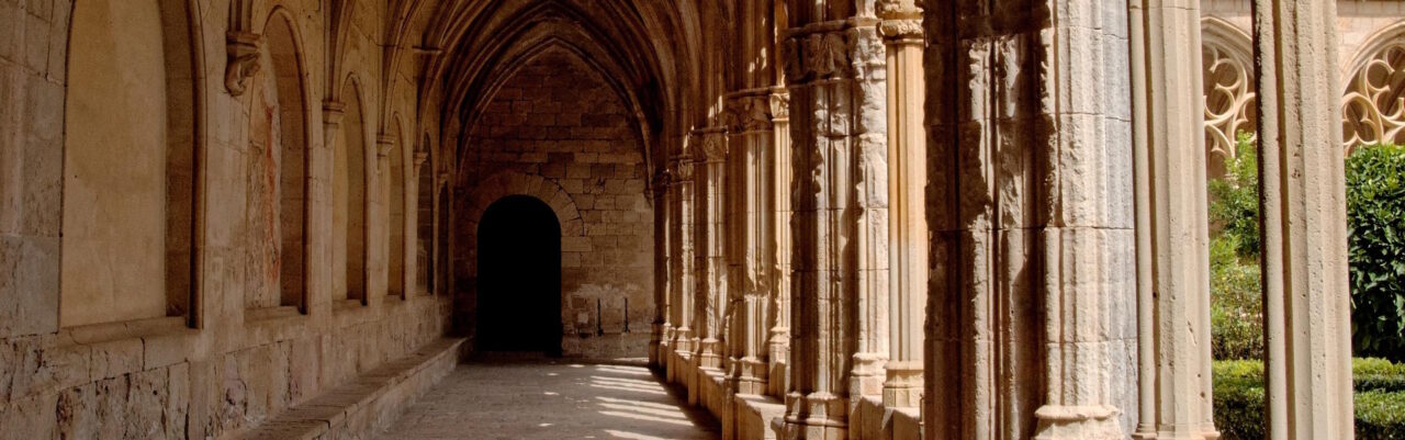 Stone cloister walkway with Gothic arches receding toward a dark doorway